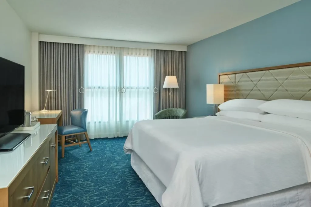 Habitaci&oacute;n con una cama grande, alfombra azul y cortinas transparentes en Walt Disney World Dolphin