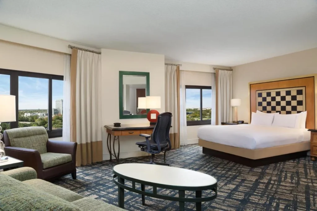 Habitaci&oacute;n con una cama grande, sof&aacute;, sill&oacute;n y ventanas de esquina en Hilton Orlando Lake Buena Vista