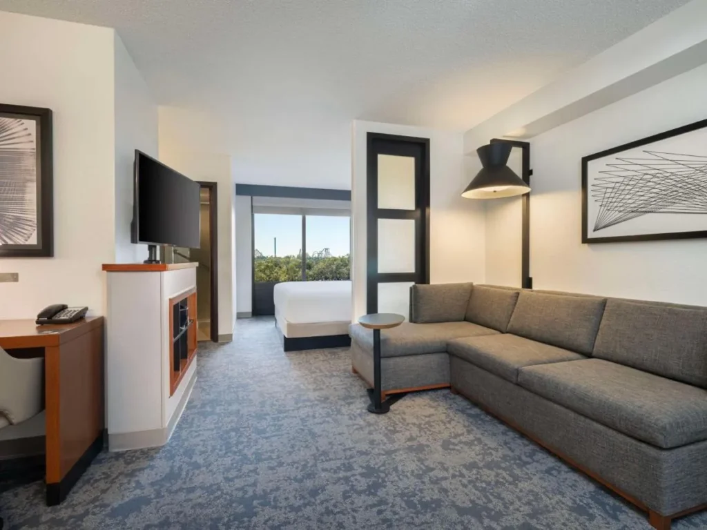 Habitación con sofá seccional y cama, montañas rusas visibles fuera, Hyatt Place Tampa/Busch Gardens