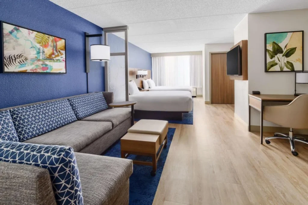 Habitaci&oacute;n con sof&aacute; seccional con acolchado azul, escritorio y camas en Hyatt Place frente a Universal