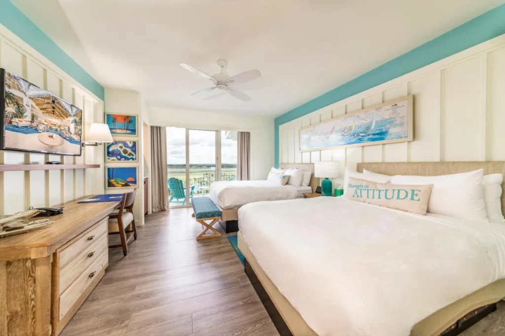 Habitación con dos camas, escritorio y balcón con sillas de color turquesa en Margaritaville Resort Orlando