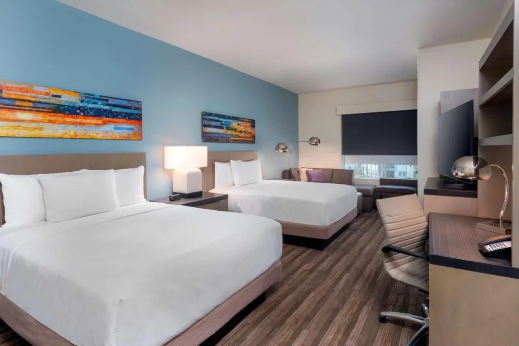 Habitaci&oacute;n con dos camas, un sof&aacute; y una pared de acento azul en Hyatt House Orlando Airport