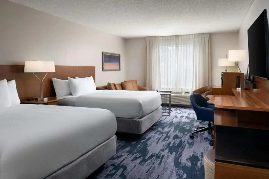 Habitaci&oacute;n con dos camas, un sof&aacute; y un largo escritorio de madera en el Fairfield Inn Orlando Airport