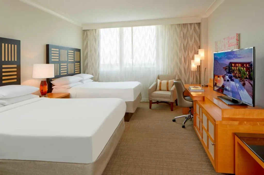 Habitaci&oacute;n con dos camas, un sill&oacute;n y un largo escritorio de madera en el Renaissance Orlando Airport Hotel