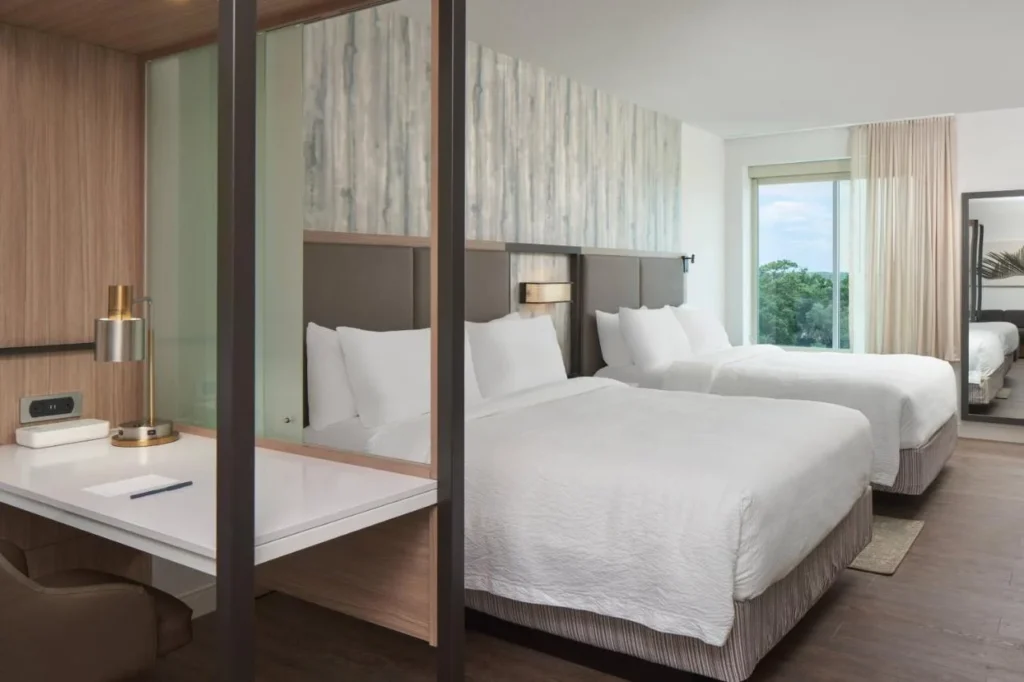 Habitaci&oacute;n con dos camas y un escritorio con paredes de vidrio en SpringHill Suites Orlando Lake Nona
