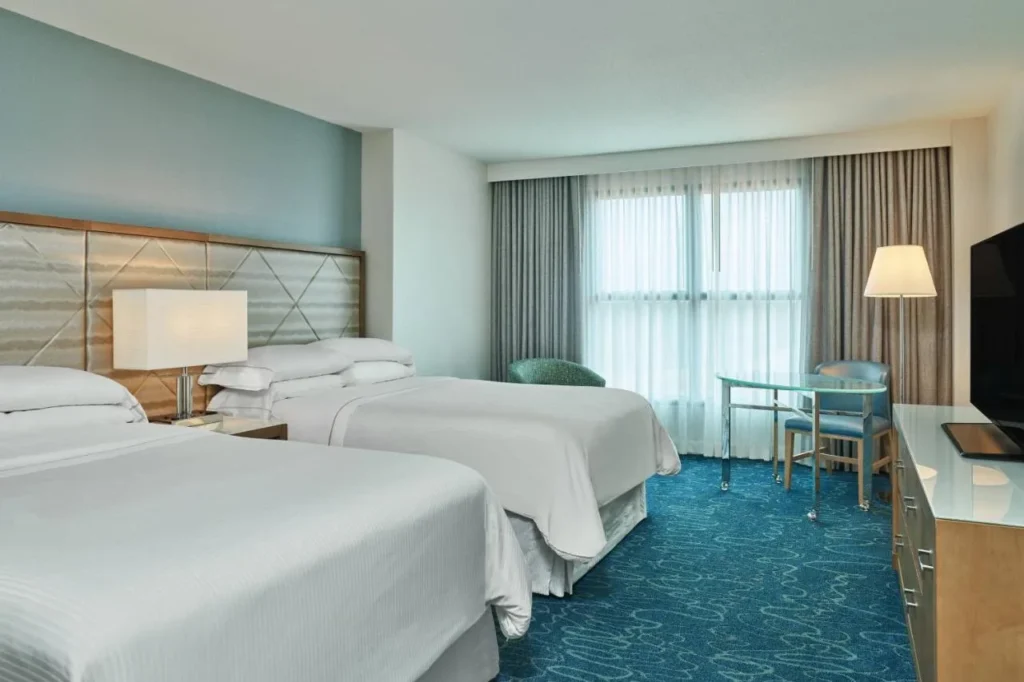Habitaci&oacute;n con dos camas, alfombra azul y una peque&ntilde;a mesa de cristal en Walt Disney World Dolphin