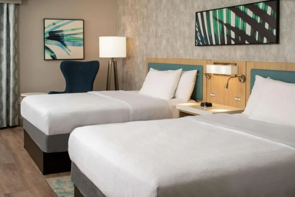 Habitaci&oacute;n con dos camas, cabeceros de color verde azulado y arte de hoja de palma en Hilton Garden Inn Orlando Airport