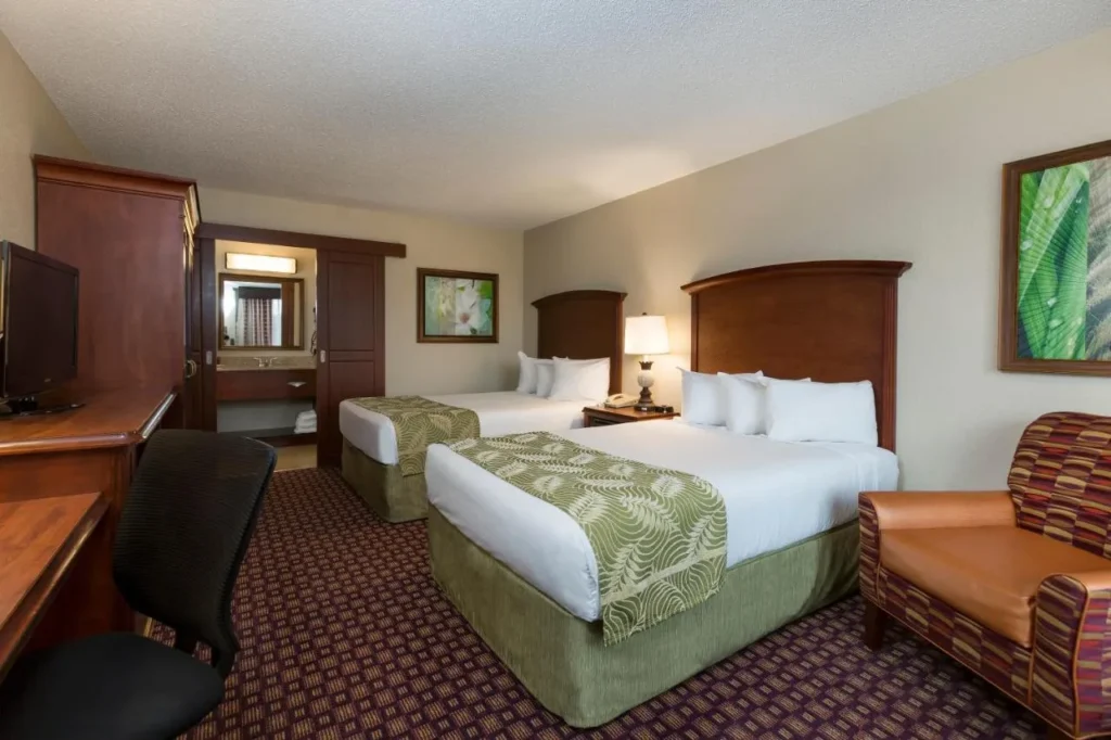 Habitación con dos camas dobles, sillón, escritorio y TV en Rosen Inn at Pointe Orlando