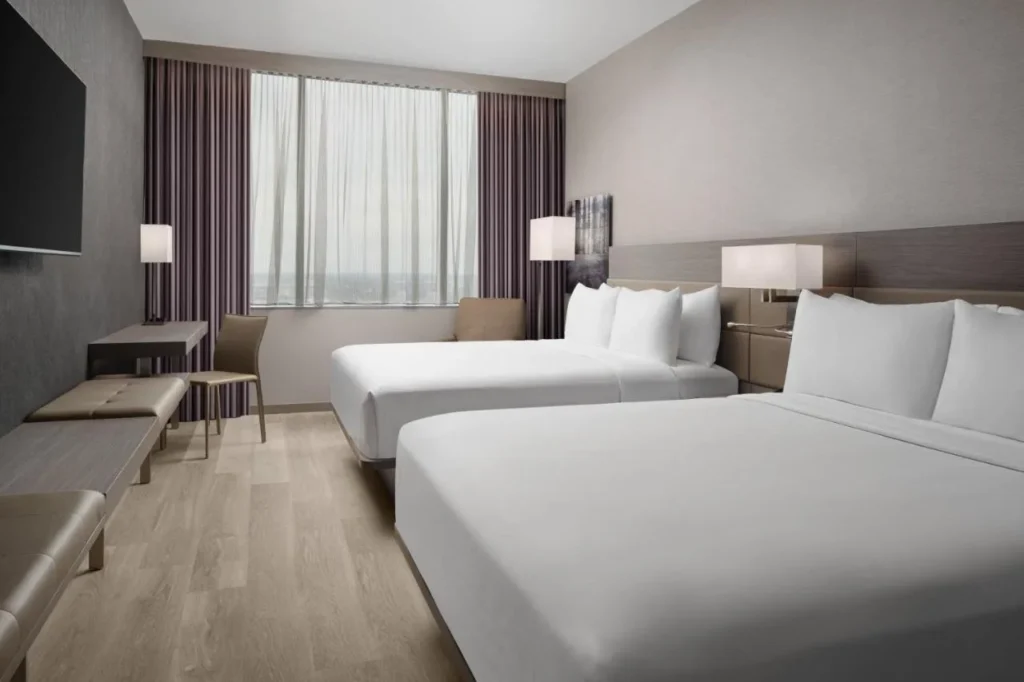 Habitación con dos camas queen, un banco y un amplio ventanal en AC Hotel Orlando Downtown