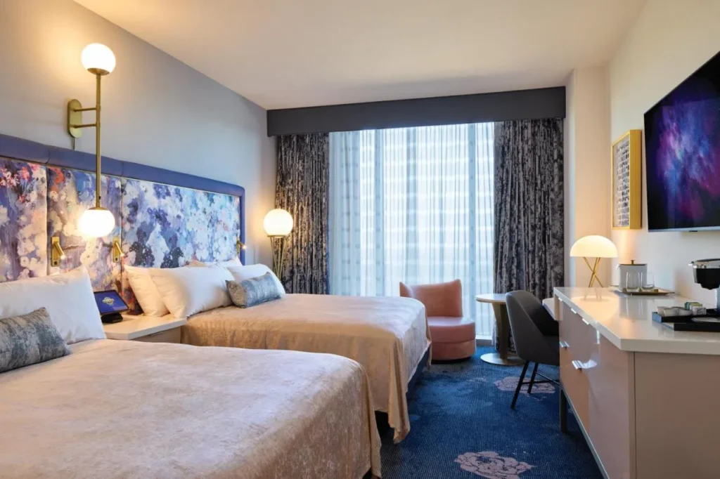 Habitación con dos camas queen, un sillón rosa y una cómoda larga en Universal Helios Grand Hotel