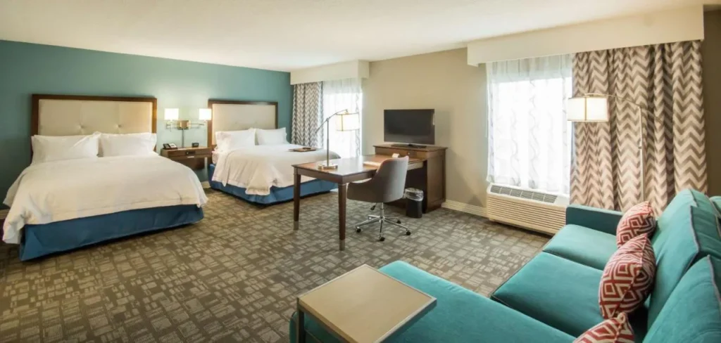 Habitaci&oacute;n con dos camas queen y un sof&aacute; de color verde azulado en Hampton Inn & Suites SeaWorld