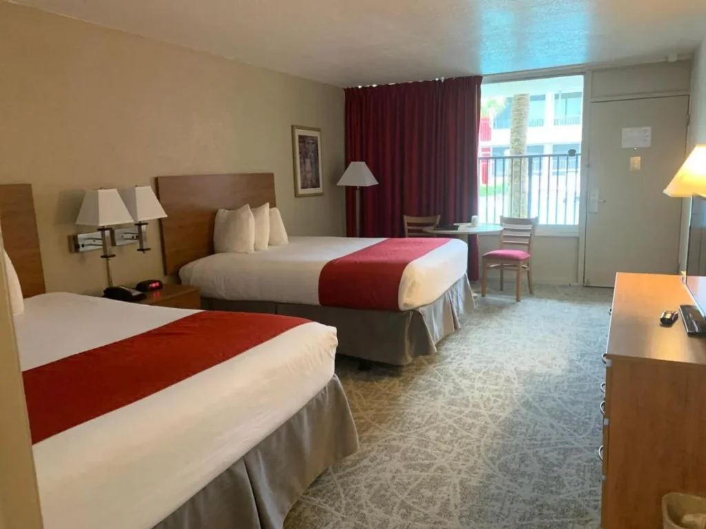 Habitaci&oacute;n con dos camas queen, mesa peque&ntilde;a y puerta de balc&oacute;n en Ramada by Wyndham Kissimmee Gateway