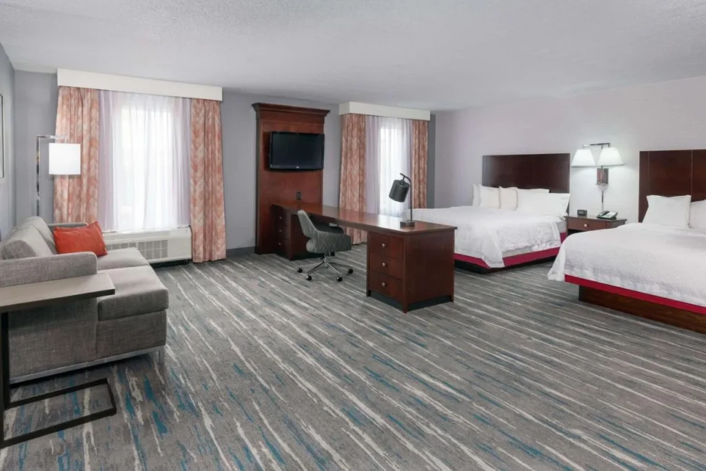 Habitaci&oacute;n con dos camas queen, sof&aacute; y escritorio largo en Hampton Inn & Suites Orlando Airport