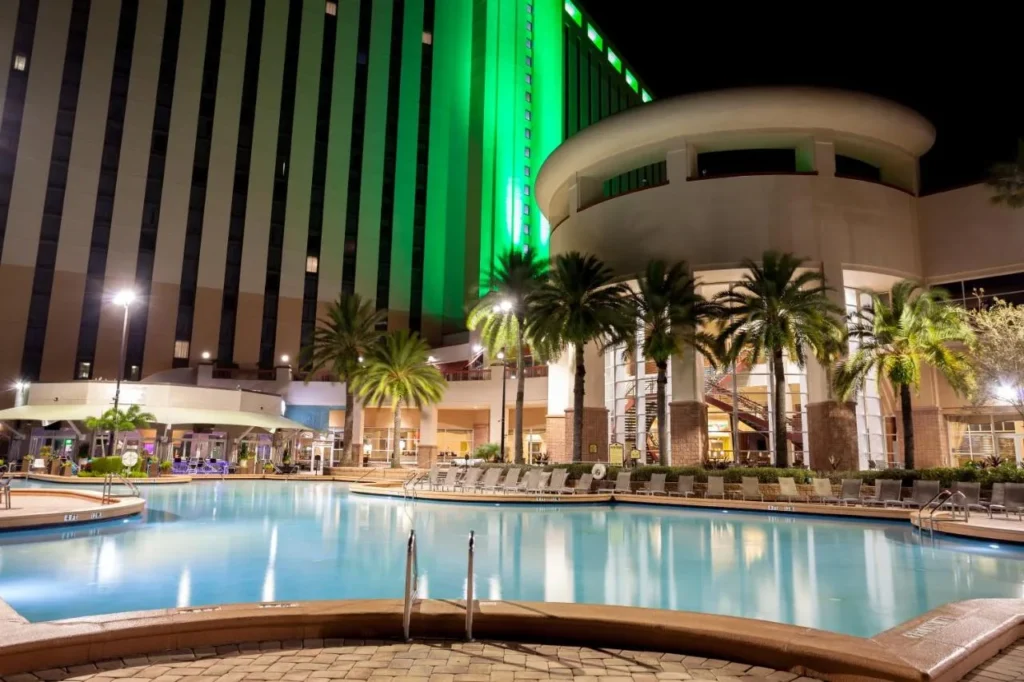 Rosen Centre Hotel piscina al aire libre por la noche con tumbonas, palmeras y la torre iluminada verde