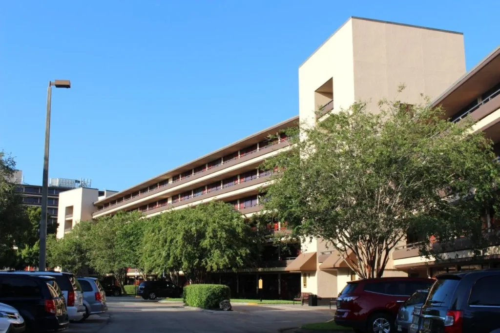 Rosen Inn at Pointe Orlando ala de invitados detr&aacute;s de &aacute;rboles frondosos, con coches en el estacionamiento