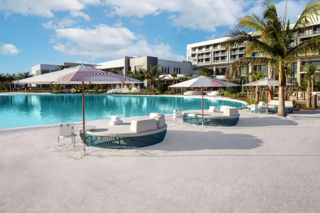 Round daybeds and striped umbrellas on white sand beside the water at Conrad Orlando