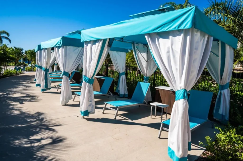 Row of poolside cabanas with turquoise canopies, white curtains and loungers at Margaritaville Resort Orlando