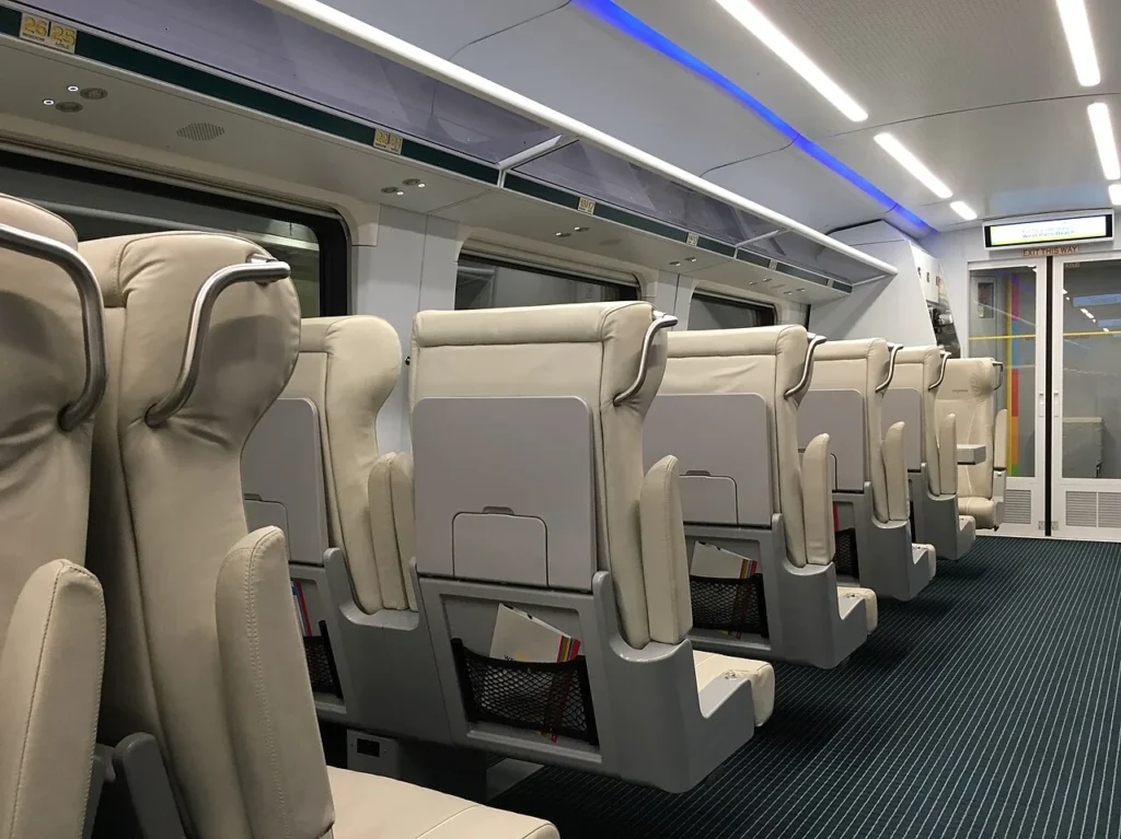Rows of cream leather reclining seats with overhead luggage racks inside a Brightline train coach
