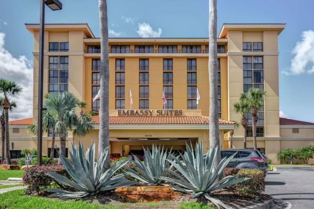 Sand-colored facade with palm trees and agave plants at Embassy Suites Orlando International Drive Convention Center