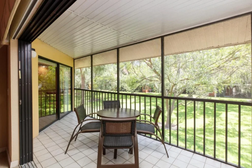 Screened balcony with a table for four overlooking lawns and oak trees at Westgate Vacation Villas