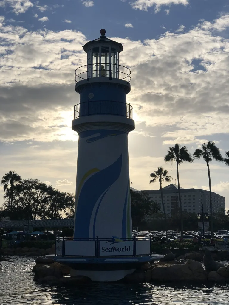 SeaWorld Orlando lighthouse by the entrance lagoon, backlit by late-afternoon sun with palms behind