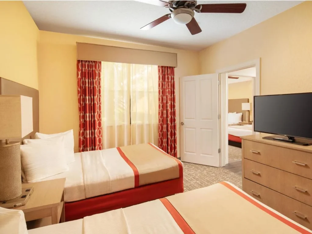 Dormitorio con dos camas, una cómoda y un televisor en una suite Floridays Resort Orlando