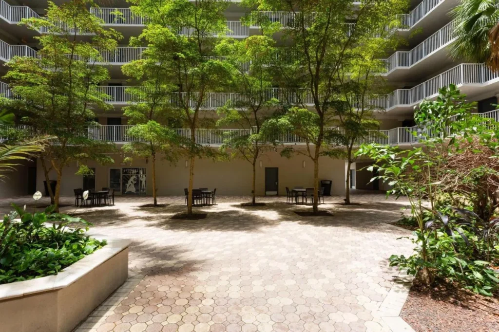 Shaded tower courtyard with trees, paved patio and tables below open-air walkways at Wyndham I-Drive Avanti