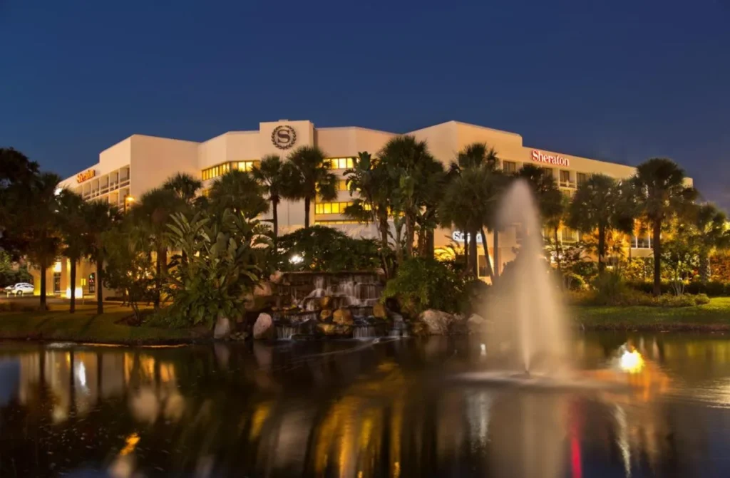 Sheraton Orlando Lake Buena Vista Resort edificio iluminado por la noche detr&aacute;s de un estanque fuente y palmeras