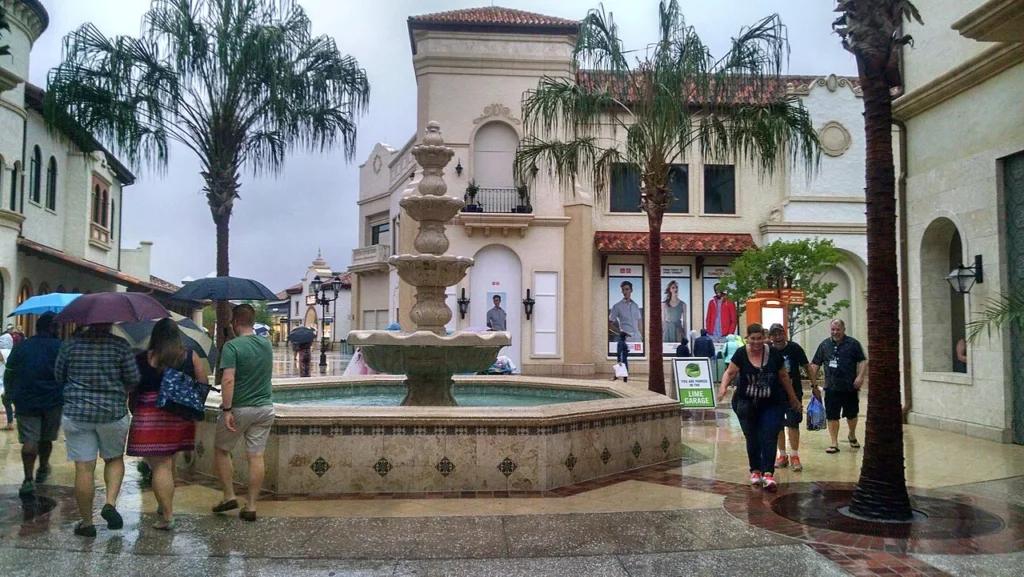 Shoppers with umbrellas walking past a tiered fountain in Disney Springs Town Center during rain