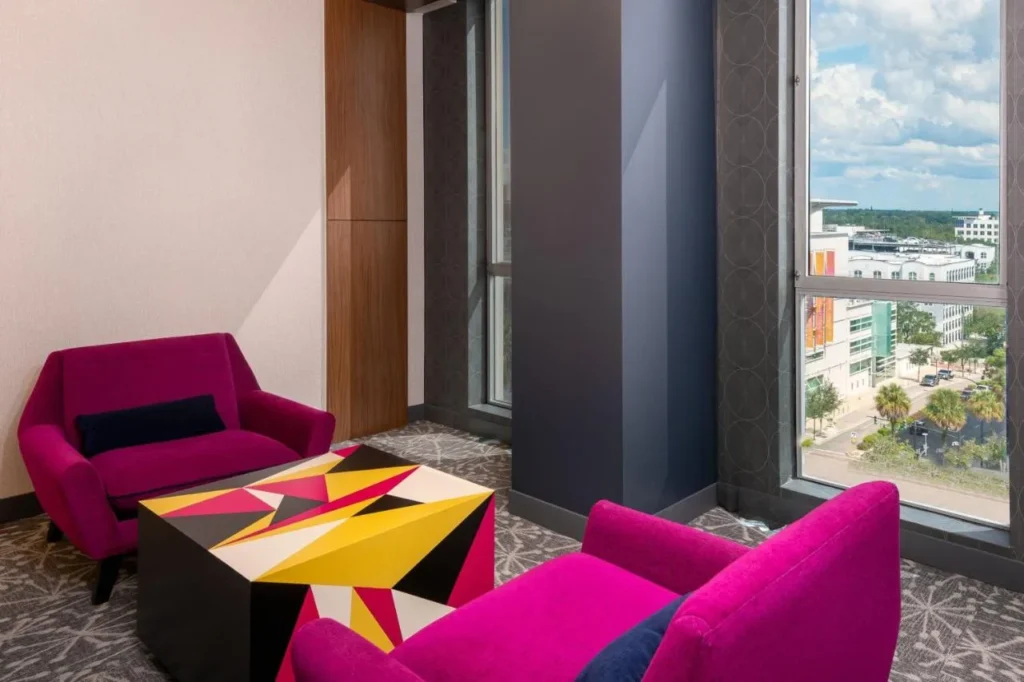Área de descanso con dos sillones rosas y una ventana sobre el centro de la ciudad en Aloft Orlando Downtown