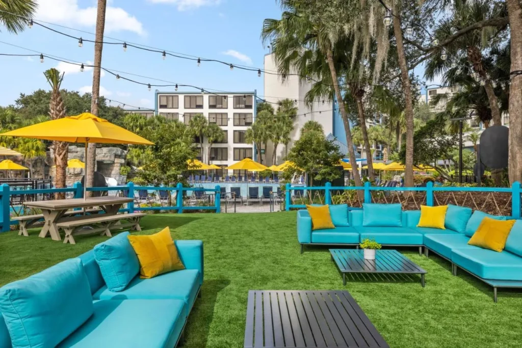 C&eacute;sped social con sof&aacute;s turquesas, mesas de picnic y luces de cuerda en Delta Hotels Orlando Celebration