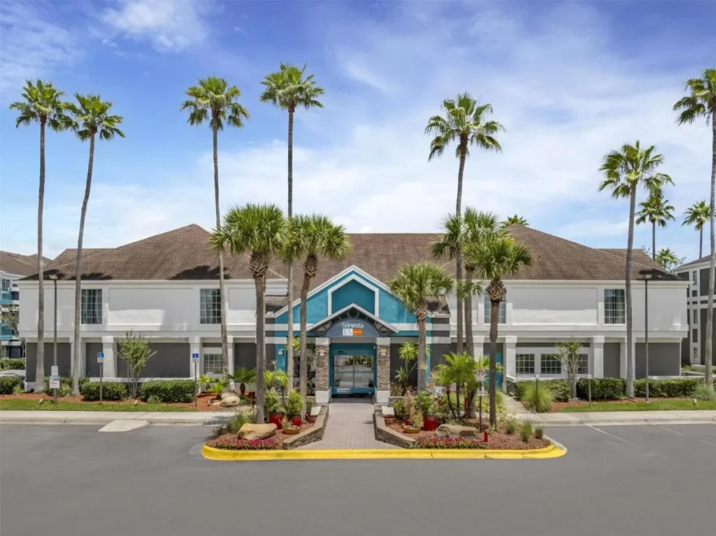 Sonesta ES Suites Orlando Lake Buena Vista entrance with tall palm trees and a blue gable