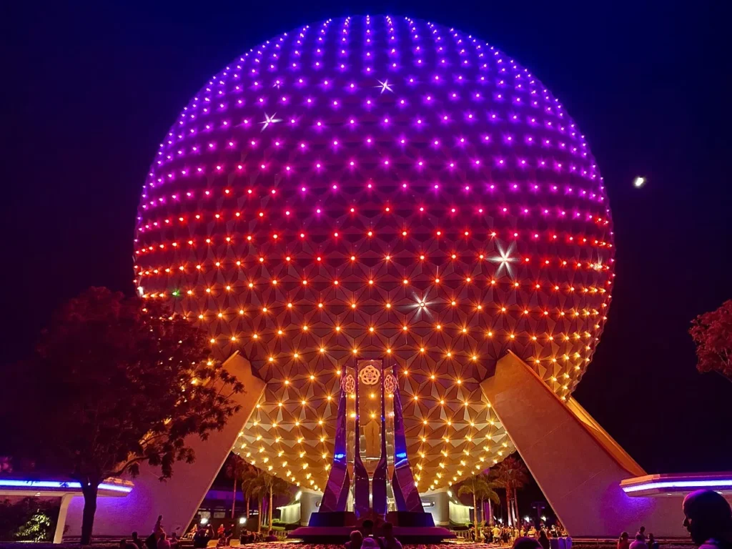 La c&uacute;pula de la Tierra iluminada de color p&uacute;rpura, rojo y oro contra el cielo nocturno en EPCOT