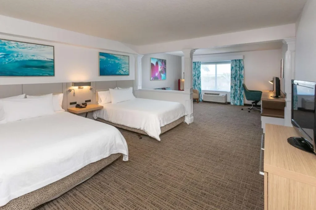 Amplia habitación con dos camas, escritorio y sala de estar en Hilton Garden Inn Daytona Beach Airport