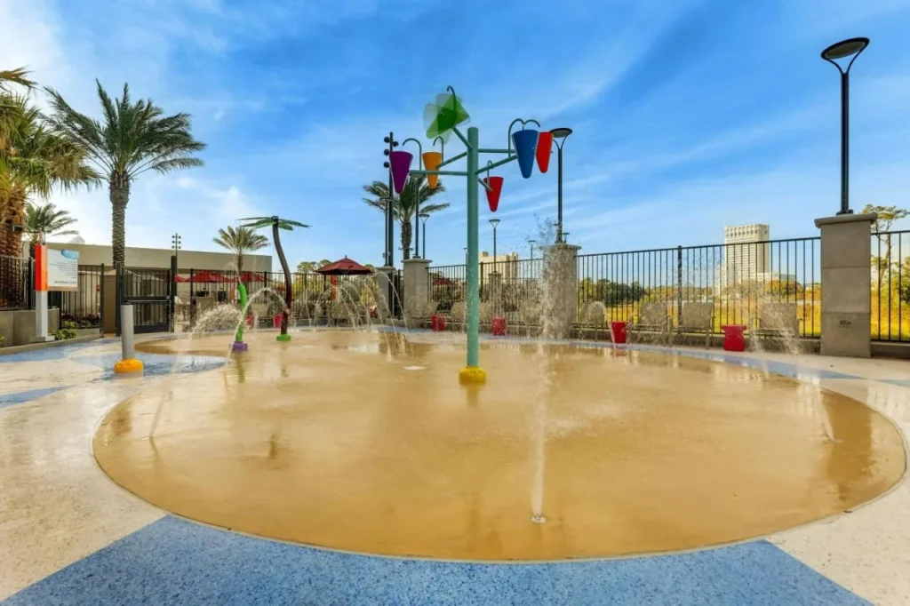 Splash pad with water jets and colorful buckets beside palm trees at Drury Plaza Hotel Orlando