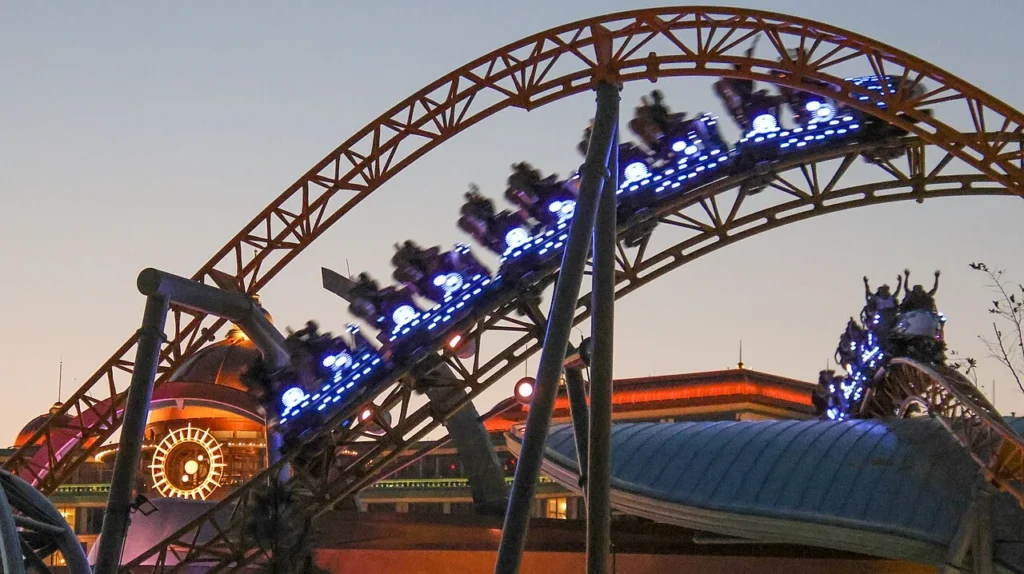 Stardust Racers trenes iluminados en azul subiendo la pista naranja en el crepúsculo en Epic Universe