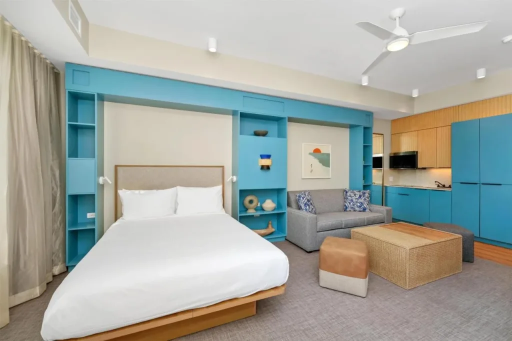 Suite tipo estudio con cama, sofá gris y cocineta azul en Embassy Suites Orlando Sunset Walk