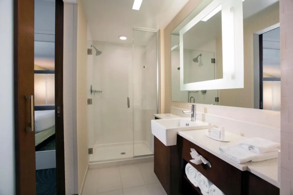 Baño en suite con ducha a ras de suelo de vidrio y espejo iluminado en SpringHill Suites Flamingo Crossings