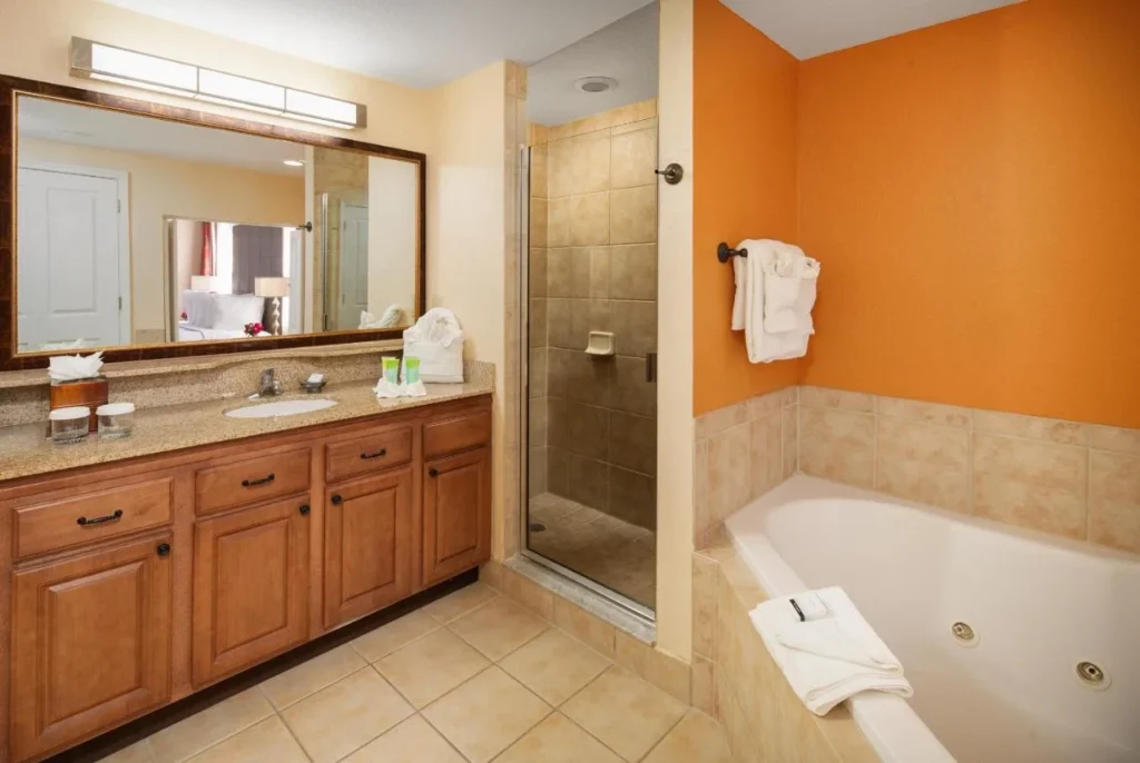 Cuarto de ba&ntilde;o con una vanidad de granito, ducha de cristal y ba&ntilde;era de hidromasaje en Floridays Resort Orlando