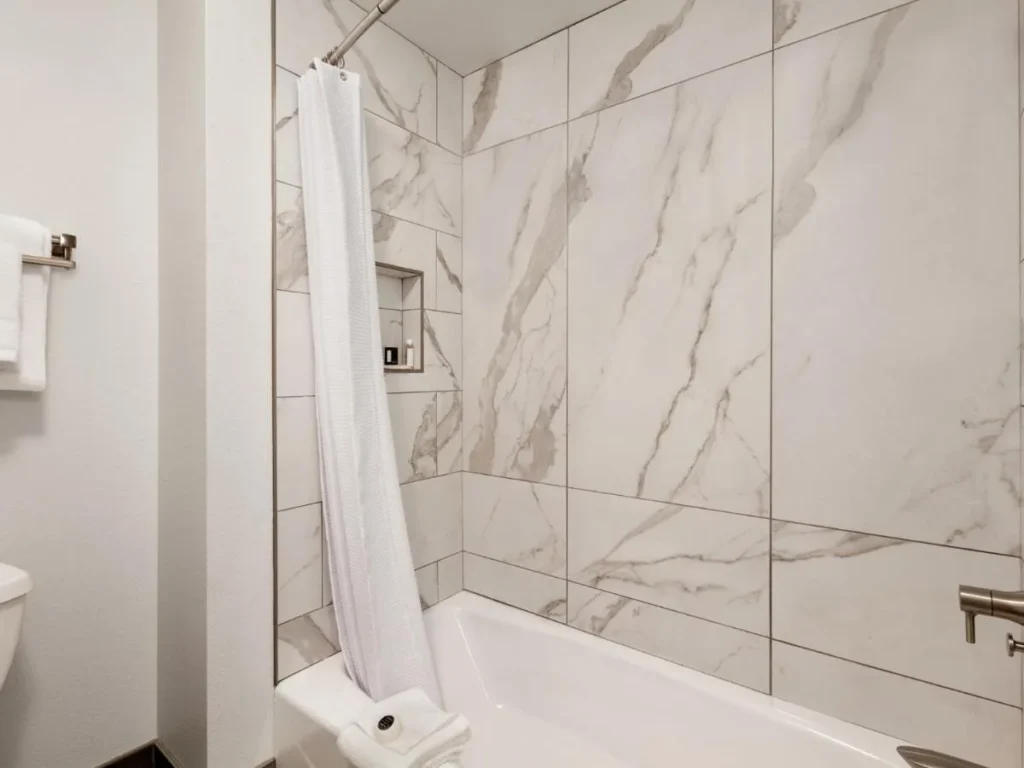 Cuarto de baño con baldosas de mármol, bañera y cortina de ducha en Buena Vista Suites Orlando