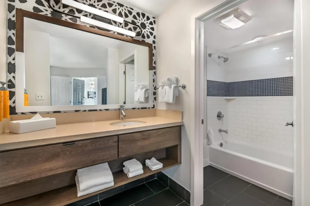 Ba&ntilde;o de la suite con tocador de madera, espejo grande y ba&ntilde;era-ducha en Sonesta ES Suites Lake Buena Vista