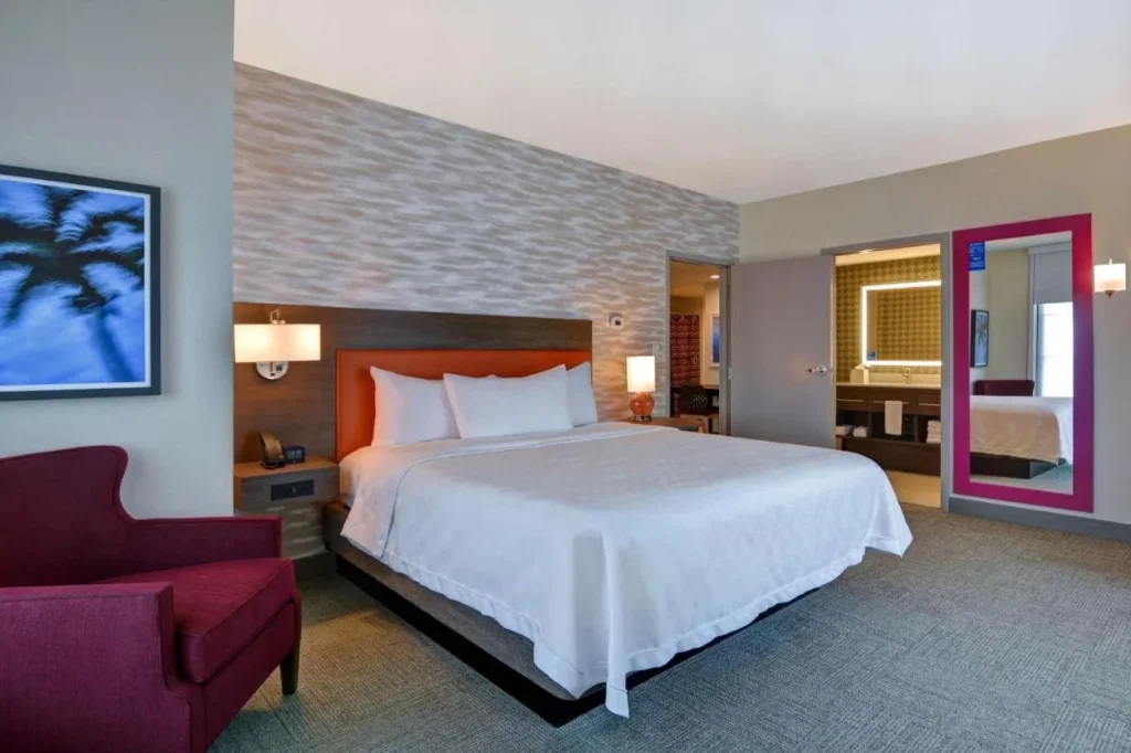 Habitación suite con cama king size, sillón rojo y puerta de baño abierta en Home2 Suites Flamingo Crossings