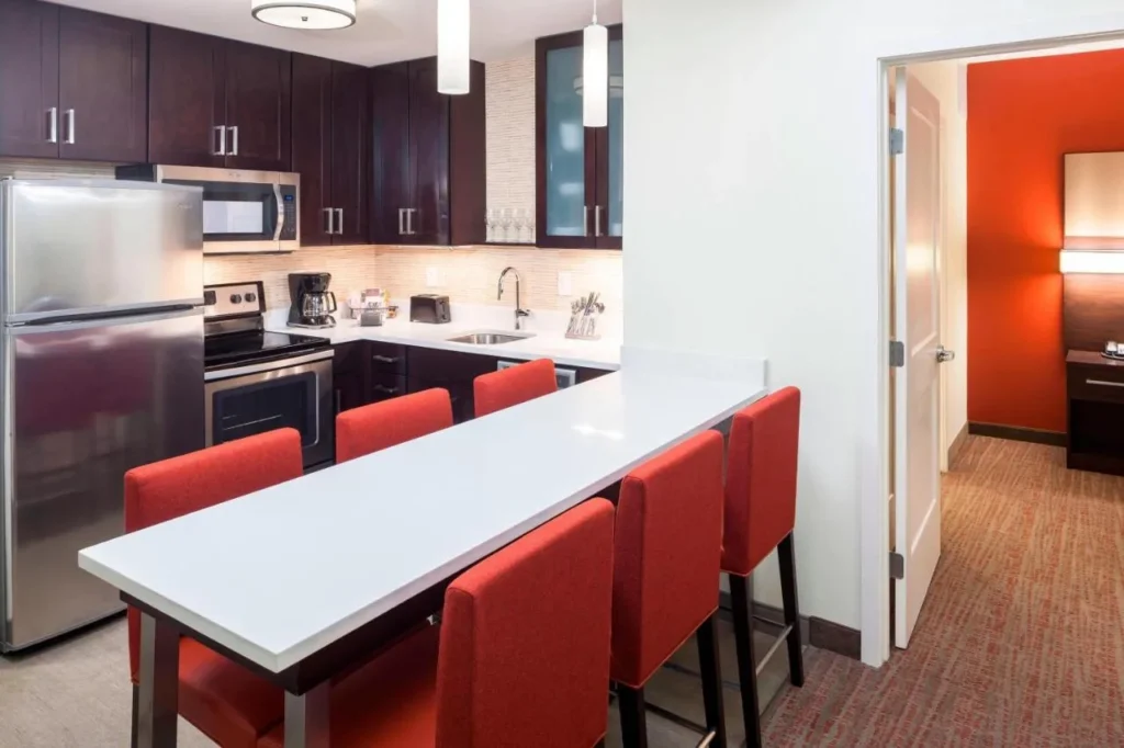 Cocina suite con barra de desayuno, taburetes rojos y puerta de dormitorio en Residence Inn Near Universal Orlando