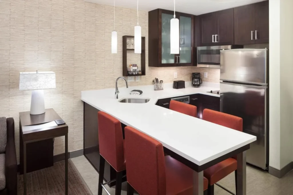 Cocina de la suite con barra de desayuno, taburetes rojos, refrigerador de acero inoxidable y microondas en Residence Inn Near Universal