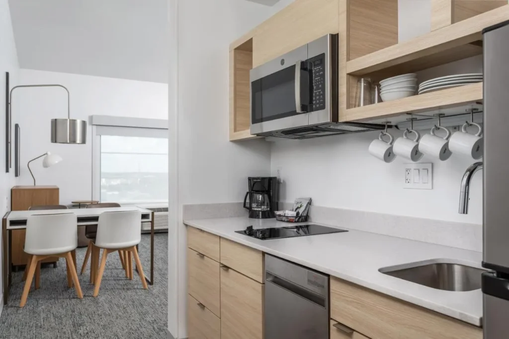 Suite kitchen with cooktop, microwave, dishwasher and dining table at TownePlace Suites Orlando Near Universal