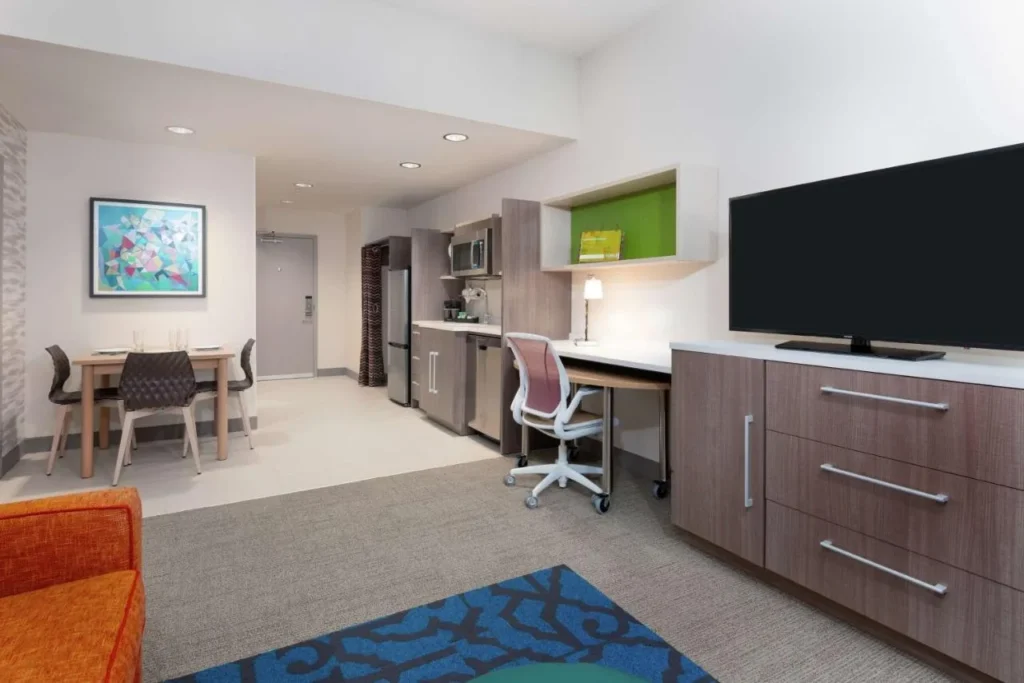 Suite kitchen with fridge, microwave, desk and dining table at Home2 Suites Orlando Near Universal