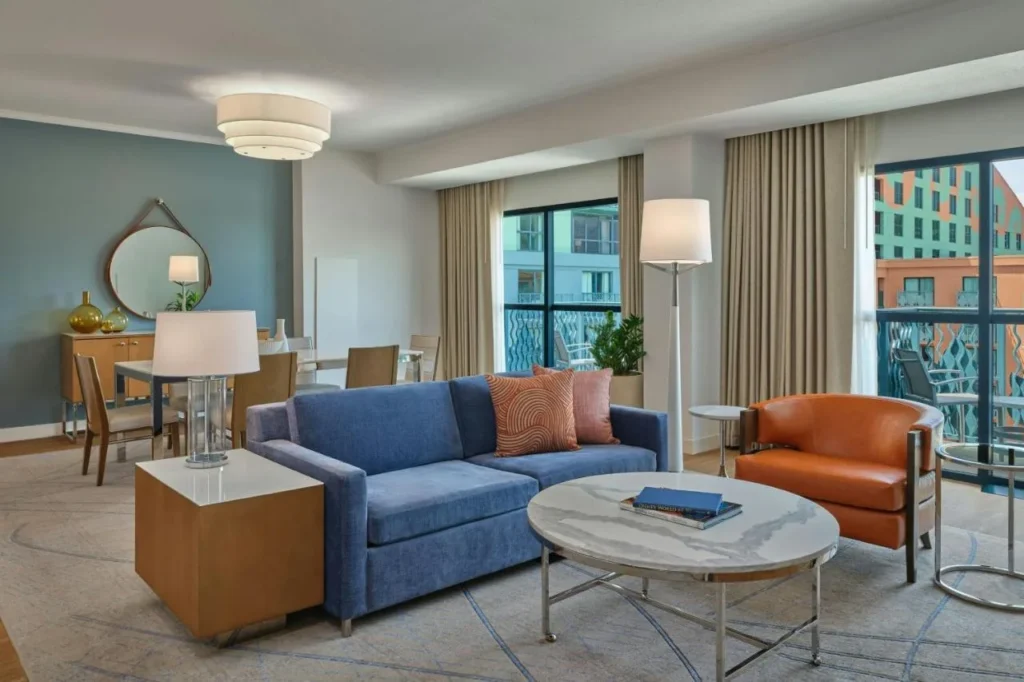 Suite living area with a blue sofa, orange armchair and balcony doors, Walt Disney World Swan