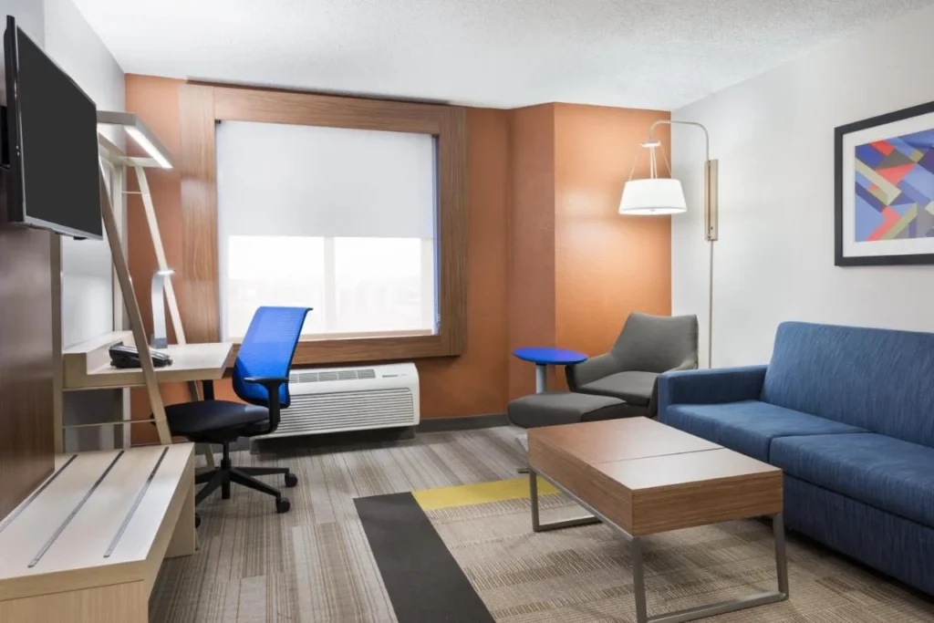 Suite living area with blue sofa, armchair and work desk at Holiday Inn Express Nearest Universal