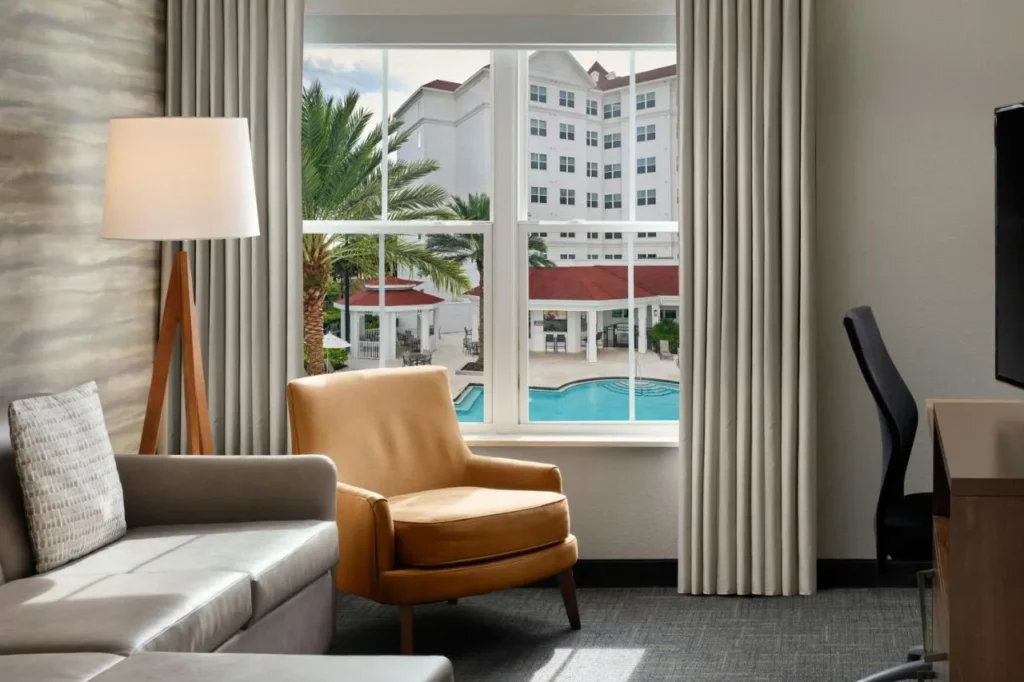 Suite con sof&aacute; y sill&oacute;n con vistas a la piscina en el Residence Inn Orlando Flamingo Crossings