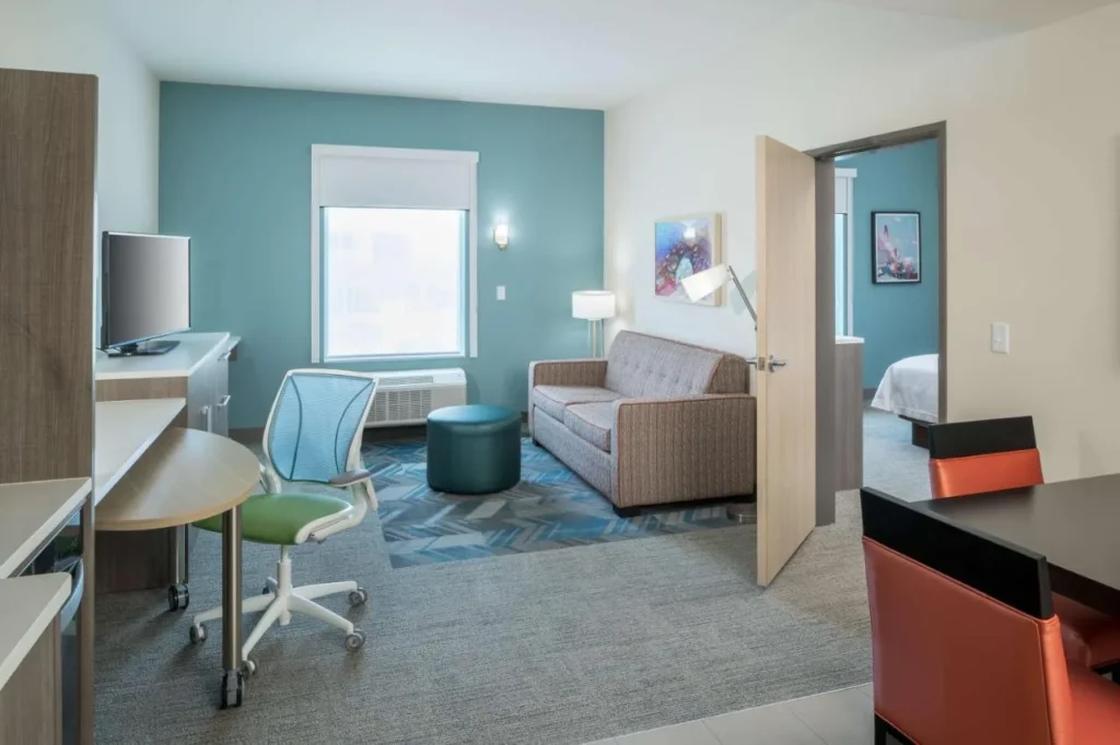 Suite living area with sofa, desk and separate bedroom at Home2 Suites Cape Canaveral Cruise Port
